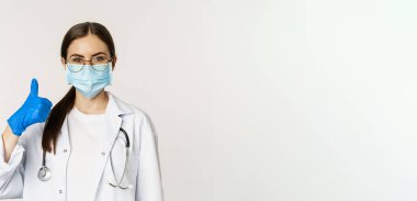 Coronavirus 'un yüz maskesi takmış kadın doktorların portresi. Baş parmaklarını gösterip gülümsüyor. Klinik ya da tıbbi web sitesi tavsiye ediyor..