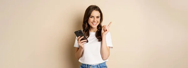 Stylish Young Modern Woman Holding Mobile Phone Pointing Finger Left — Photo