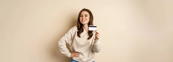 快乐的女性顾客展示信用卡 微笑满意 站在米色背景之上 — 图库照片