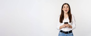 Young woman with smartphone, smiling and looking at camera, using mobile phone app, cellular technology and online shopping concept, white background.