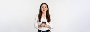 Akıllı telefonlu genç bir kadın, gülümsüyor ve kameraya bakıyor, cep telefonu uygulaması, cep telefonu teknolojisi ve online alışveriş konsepti kullanıyor, beyaz arka plan.