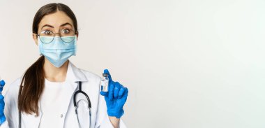 Covid-19 aşı ve sağlık hizmeti konsepti. Tıbbi maskeli genç doktor beyaz arka planda duran Coronavirus omicron varyasyonundan şırınga ve aşı gösteriyor..