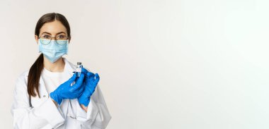 Genç kadın portresi, tıbbi maske ve üniformalı doktor, aşıyı gösteriyor, covid-19 aşı kampanyası, beyaz arka planda duruyor..