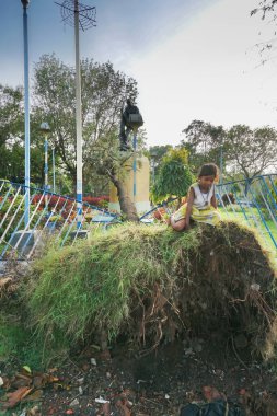 Kolkata, Batı Bengal, Hindistan - 28 Mayıs 2020: Kız çocuklar Mahatma Gandhi heykelinin önünde süper kasırga Amphan tarafından sökülmüş bir ağaçta oynuyorlar. Yıkım sonrası hayat yeniden yükseliyor..