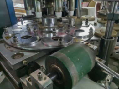 Kağıt bardakların bulanık görüntüsü kağıttan yapılıyor, kağıt bardak üretim makineleri kullanılarak, çalışan bir bardak imalatı veya üretim ünitesi görünümünde.