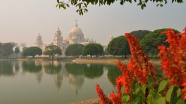 Victoria Memorial 'ın 4K stok videosu, Orta Kolkata, Batı Bengal, Hindistan' da büyük bir mermer bina. Orta alandaki göl suyunun yansıması. Çerçevenin sağ tarafında kırmızı çiçekler var..
