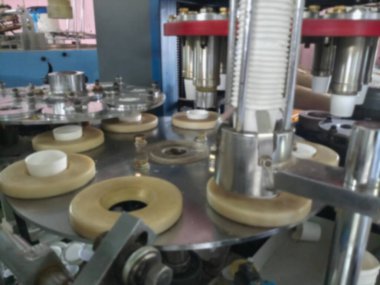 Kağıt bardakların bulanık görüntüsü kağıttan yapılıyor, kağıt bardak üretim makineleri kullanılarak, çalışan bir bardak imalatı veya üretim ünitesi görünümünde.