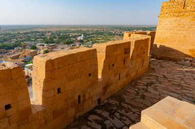 Jaisalmer, Rajasthan, Hindistan - 13 Ekim 2019: Jaisalmer Kalesi veya Altın Kale 'nin büyük duvarları, sarı kumtaşından yapılmış, sabah ışığında şehrin bir kısmı çerçevede. UNESCO dünya mirası sahası.