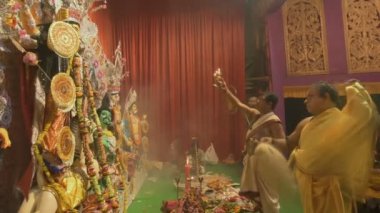 Kolkata, Hindistan -13 Ekim 2021: Hindu rahipler Tanrıça Durga 'ya panchpradip, kutsal lamba ve chamor ile tapıyorlar. Ashtami puja aarati - kutsal Durga Puja ritüeli - renkli ışığın altında geceleyin çekildi.