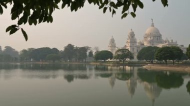 Kolkata 'daki büyük mermer bina Victoria Memorial' ın 4K stok videosu, Kolkata 'nın ünlü anıtı, Batı Bengal, Hindistan. Binanın tepesinin ön plandaki göl suyunun yansıması..