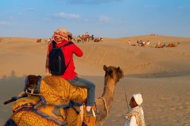 Thar Çölü, Rajasthan, Hindistan-15 Ekim 2019: Cameleer, tatlı, Camelus dromedarius 'u kum tepelerine çeken dişi turistlere bakıyor. Deve binmek gezginler için popülerdir..