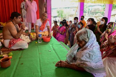 Howrah, Batı Bengal, Hindistan - 14 Ekim 2021: Yaşlı Bengalli dul tanrıça Durga 'ya taparken Hindu Purohit Hindu dindarlar için Sanskritçe shlokas söylerken tanrıçaya pejali sundu.