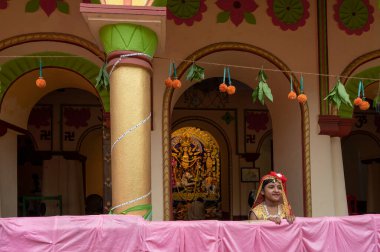 Howrah, Hindistan -26 Ekim 2020: Bengalli kız çocuğu şenlikli elbiseler içinde, arka planda Tanrıça Durga ile gülümsüyor ve poz veriyor, yaşlılığın içinde dekore edilmiş ev. Durga Puja, en büyük Hinduizm festivali..