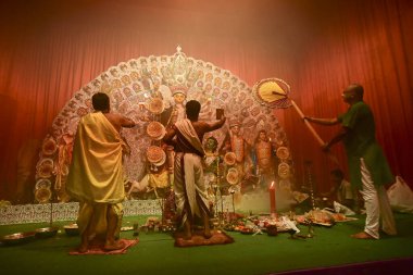 Howrah, India -October 13, 2021 : Hindu Priests worshipping Goddess Durga with mirror, ghanta, chamor and hand fan. Ashtami puja aarati - sacred Durga Puja ritual - shot at night.