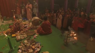 Howrah, India- October 15th, 2021 : Hindu devotees worshipping Goddess Durga with folded hands on Sandhi Puja, the sacred juncture of Ashtami and Nabami, as ritual. Holy 18 lamps are lit.