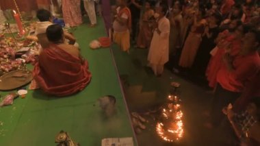 Howrah, India- October 15th, 2021 : Hindu devotees worshipping Goddess Durga with folded hands on Sandhi Puja, the sacred juncture of Ashtami and Nabami, as ritual. Holy 18 lamps are lit.