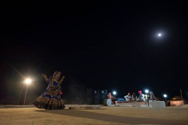 Thar desert, Rajasthan, India - October 15th 2019 : Rajasthani female dancer dancing, dressed with cultural dress of Rajasthan, at night. Musicians are playing music instruments in moonlit night.