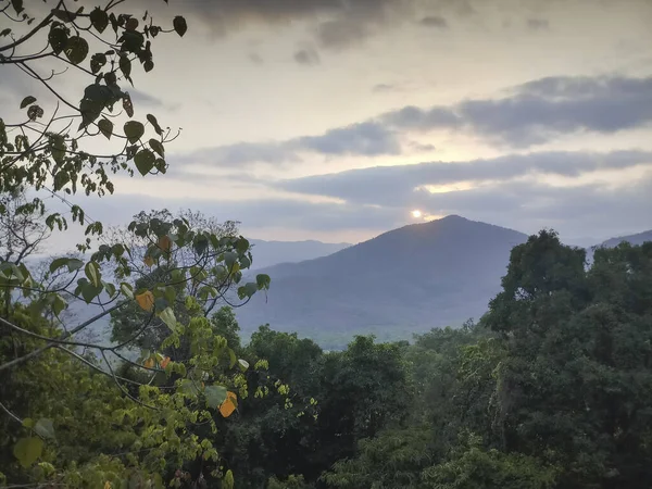 Sunset seen from viewpoint with cloudy sunset sky, distant mountains in the background and forest in the foreground. Karnataka, India.