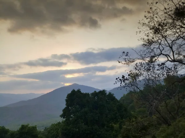 Sunset seen from viewpoint with cloudy sunset sky, distant mountains in the background and forest in the foreground. Karnataka, India.