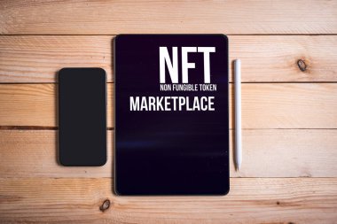 Ahşap masa üzerinde NFT pazarının duvar kağıdı olan bir tablet. Finanse edilemeyen jetonla çalışmak için cep telefonu. Finanse edilemez sembol konseptiyle para kazanmak.