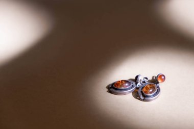 Silver earrings with amber on soft brown background. Still life and creative photo with shadows.