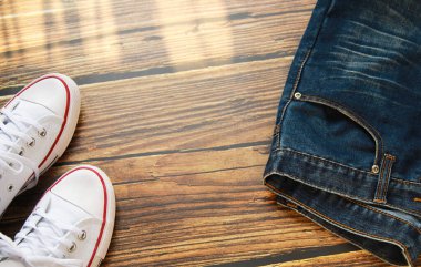 Koyu eski ahşap arka planda mavi kot pantolon ve beyaz spor ayakkabının yakın çekim görüntüsü.