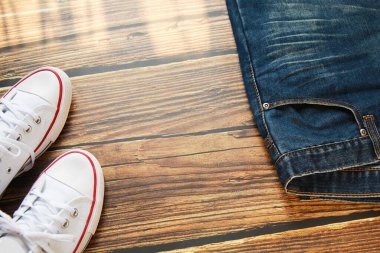 Koyu eski ahşap arka planda mavi kot pantolon ve beyaz spor ayakkabının yakın çekim görüntüsü.