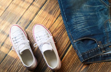 Koyu eski ahşap arka planda mavi kot pantolon ve beyaz spor ayakkabının yakın çekim görüntüsü.