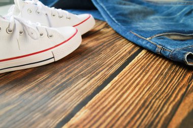 Koyu eski ahşap arka planda mavi kot pantolon ve beyaz spor ayakkabının yakın çekim görüntüsü.