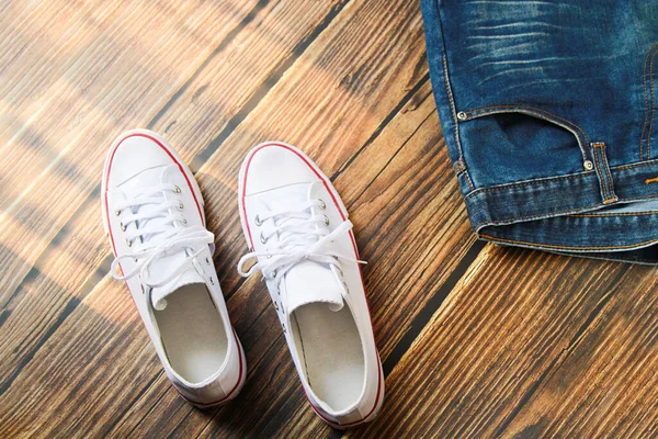 Koyu eski ahşap arka planda mavi kot pantolon ve beyaz spor ayakkabının yakın çekim görüntüsü.