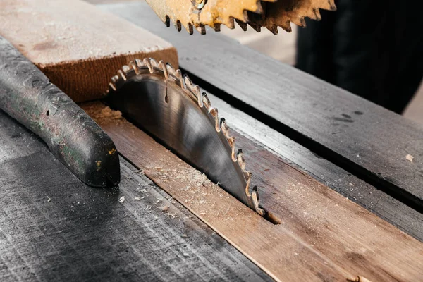 The blade of a circular saw on the desktop cuts a pine board.