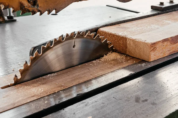The blade of a circular saw on the desktop cuts a pine board.
