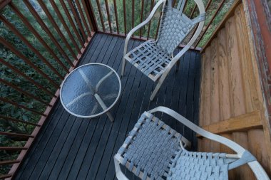 Yuvarlak bir masanın yanında cam kaplama ve ahşap kaplama arka planı olan bir çift sandalye.