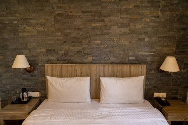 Beyaz çarşaflı, yastık kılıflı ve duvarına lambalar takılmış bir yatak.