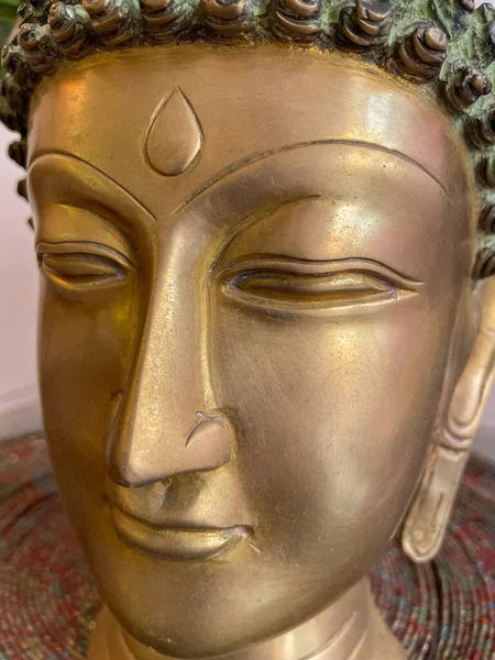 A close-up image of a golden Buddha face made of brass