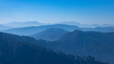 A panoramic view of mountain silhouettes with mist and clear blue sky