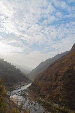 Dar bir vadiden akan bir nehrin manzarası. Ufukta bulutlar ve mavi gökyüzü ile dağılmış taşlar ve kayalar.