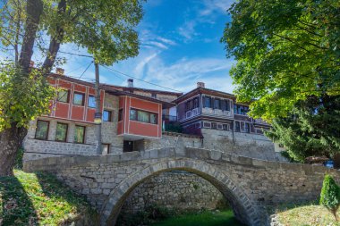 Güzel yeşil çimenleri ve mavi gökyüzü olan antik taş köprü. Arka planda geleneksel Bulgar evleri