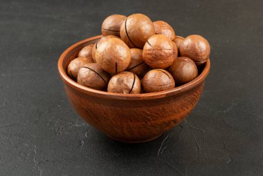 Macadamia fındıkları bir kasede, koyu bir arka planda.