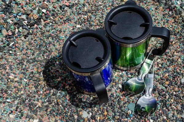 Metal termo bardaklar ve deniz taşları üzerinde kaşıklar.