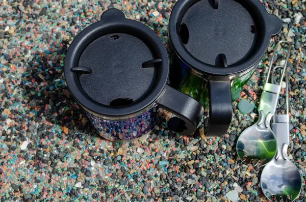 Metal termo bardaklar ve deniz taşları üzerinde kaşıklar.