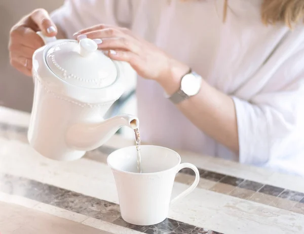 a young woman pours tea from a beautiful white teapot into a ceramic cup