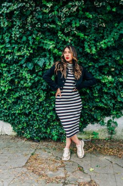 Uzun sarı saçlı latin genç kadın, ceketli, hayat tarzlı, arka planda doğayla iç içe olan, günlük, uzun elbiseler giyiyor.