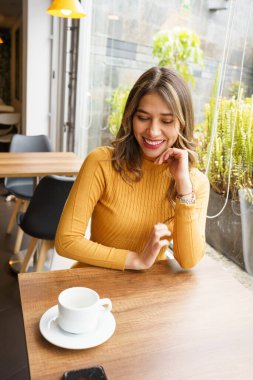 Güzel, latin, dalgalı sarı saçlı genç bir kadın sıcak bir içkinin tadını çıkarıyor, şehirde güzellik ve yaşam tarzı, kahve molası.