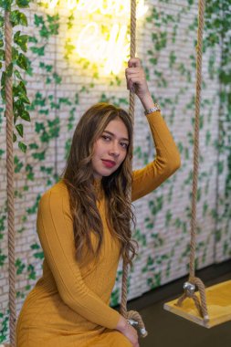 Sarı saçlı, makyajlı, günlük moda elbisesi, güzellik ve yaşam tarzı modelli, iç dekorasyonlu, salıncakta sallanan genç bir Latin kadının üzerinde oturuyordu.