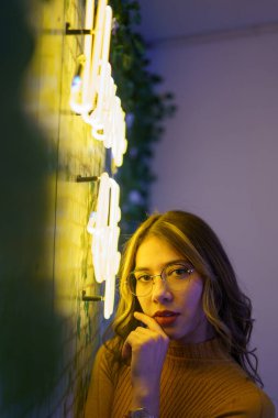 Güzel, genç, dalgalı saçlı, yüzünde makyaj ve gözlüklerle poz veren, dekorasyon, güzellik ve aksesuarlı karanlık bir yer olan Latin bir kadının yüzü.