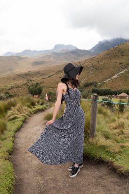 Doğada yürüyüş yapan genç bir Latin kadın, şapka ve uzun bir elbise giyiyor, yaşam tarzı ve özgürlüğün tadını çıkarıyor.