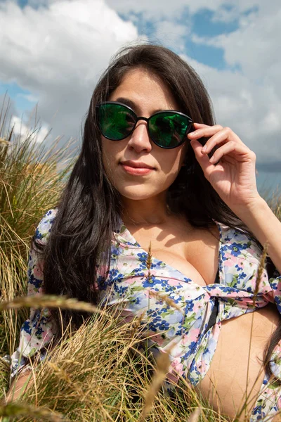 Uzun düz saçlı, güneş gözlüklü, renkli bluzlu, açık hava arka planlı, yaz günlerinde güzellik ve yaşam tarzı olan Latin bir kadının yüzünün detayları.