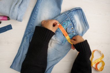 Bir dikiş atölyesinde çalışıyorum. Renkli ipliklerin yanında bir kot kumaşı tamir etmeye çalışıyorum. Çalıştığım aletlerle dikiş atölyesinde çalışıyorum.