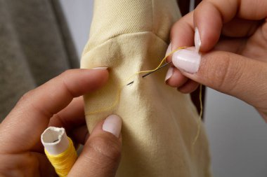 Bir terzinin elinin ayrıntıları iğne ve iplikle ceket dikmesi, stüdyoda moda işi, kıyafet stili ve onarımı.